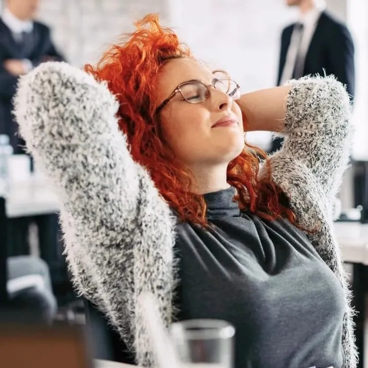 Femme détendue, les mains derrière la tête, assise à son bureau