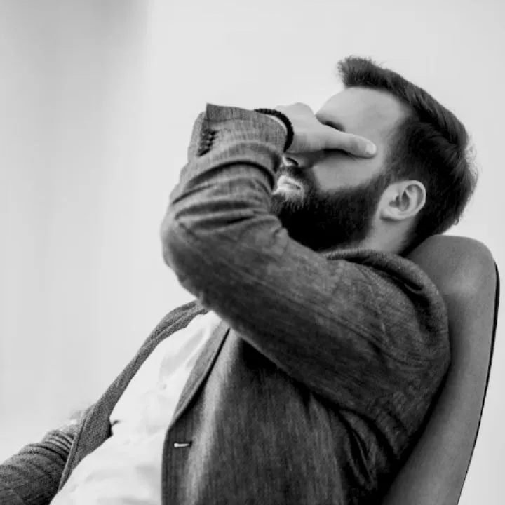 Homme épuisé, la main sur le visage, assis sur une chaise de bureau, photo en noir et blanc